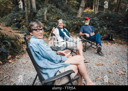 Portrait von Freunden Getränke in beim Sitzen auf Stühlen im Wald Stockfoto