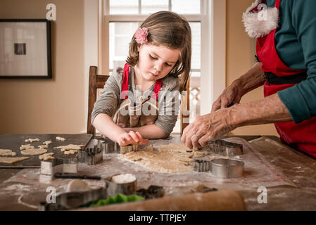 Enkelin hilft Großmutter, weihnachtskekse auf dem Tisch zu machen Stockfoto