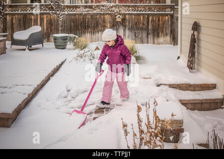 Volle Länge des Mädchens Entfernen von Schnee im Hinterhof abgedeckt im Winter Stockfoto