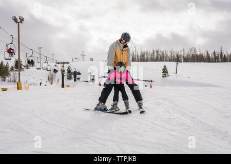 Vater mit Tochter Skifahren auf schneebedeckten Landschaft gegen bewölkter Himmel Stockfoto