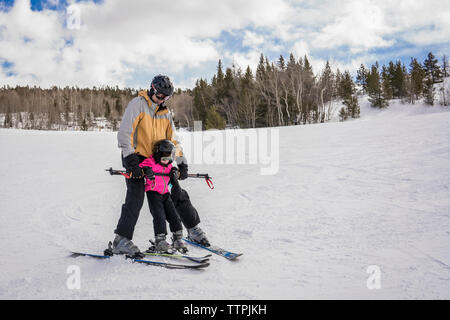 Vater mit Tochter Skifahren auf schneebedeckten Landschaft gegen bewölkter Himmel im Wald Stockfoto