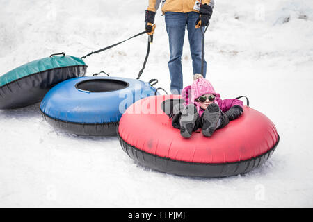 Mittelteil des Vaters rodeln Tochter auf schneebedeckten Feld Stockfoto