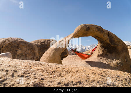 Frau entspannen auf der Hängematte aufhängen von Rock Formation gegen den klaren blauen Himmel Stockfoto