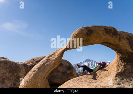 Weibliche Wanderer liegen auf Rock Formation gegen den blauen Himmel Stockfoto