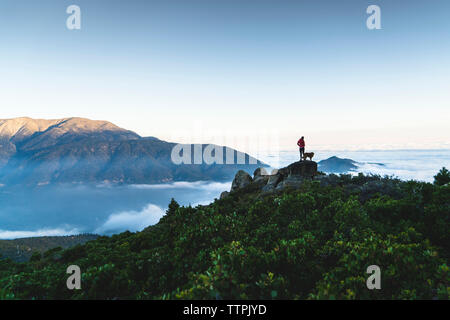 Fernsicht auf Frau mit Hund steht an der Spitze des Berges von cloudscape Stockfoto