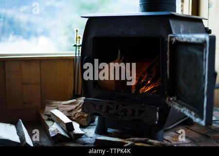 Nahaufnahme der Holzofen durch Fenster auf Parkett im Cottage Stockfoto