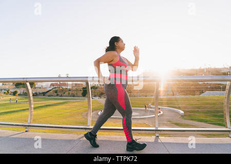 Seitenansicht der Frau joggen auf erhöhten Laufsteg gegen den klaren Himmel Stockfoto