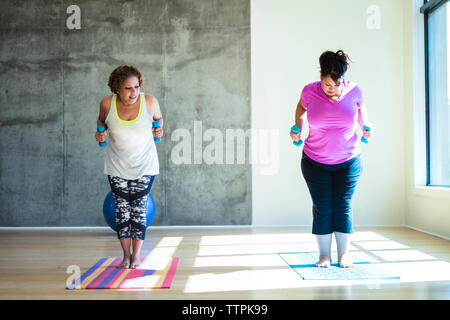 Frau auf der Suche nach Freund stehend auf trainingsmatte halten Hanteln gegen die Wand im Yoga Studio Stockfoto