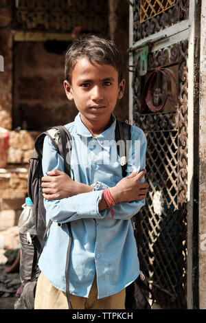 Porträt der jungen mit verschränkten Armen und Rucksack tragen Schuluniform durch Tor gegen Haus Stockfoto