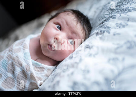 Cute Baby Mädchen aufgewickelt in der Decke weg schauen beim liegen auf dem Bett Stockfoto