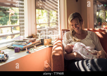 Glückliche Mutter bei neugeborenen Tochter während ihrer Durchführung auf Stuhl zu Hause Stockfoto