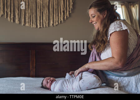 Lächelnde Mutter einwickeln neugeborenen Tochter mit Decke auf dem Bett zu Hause. Stockfoto