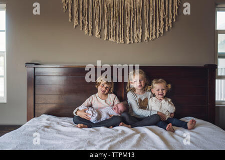 Portrait von lächelnden Schwestern mit Baby Mädchen sitzen auf dem Bett zu Hause. Stockfoto