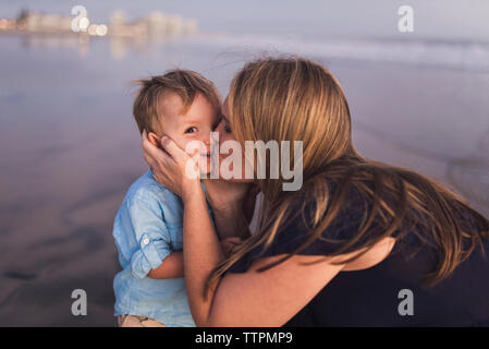 Glückliche Mutter küssen Sohn am Strand bei Sonnenuntergang Stockfoto