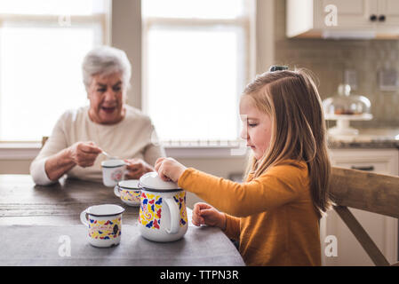 Enkelin und große Großmutter in der Küche spielen mit Tee Set Stockfoto