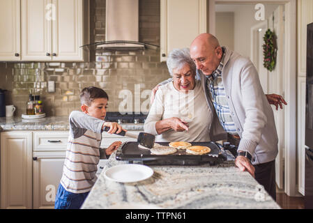 Erwachsener Sohn umarmen Mutter beim Kochen Pfannkuchen mit jungen Enkel Stockfoto