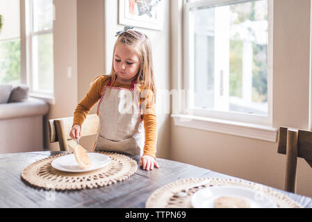 Kleines Mädchen in Schürze flipping Pfannkuchen zum Frühstück Tabelle Stockfoto