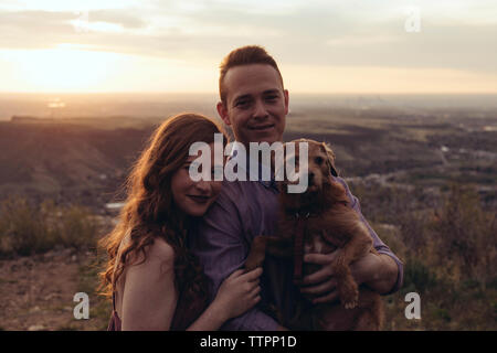 Portrait von junges Paar mit Hund stehend auf dem Feld bei Sonnenuntergang Stockfoto
