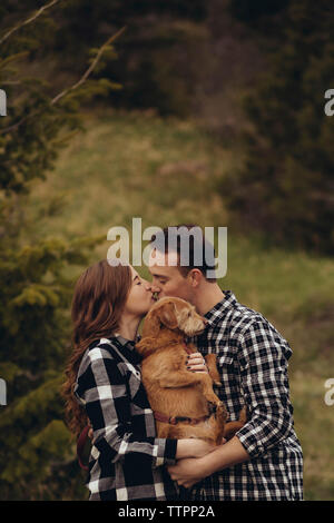 Junges Paar mit Hund beim Küssen auf den Mund Stockfoto