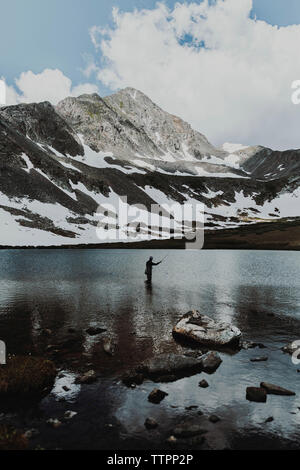 Mitte der Abstand der Mann angeln beim Stehen in der See gegen Berge im Winter Stockfoto