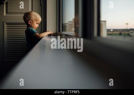 Seitenansicht des Jungen spielen mit Spielzeug Autos auf Fensterbank zu Hause bei Sonnenuntergang Stockfoto