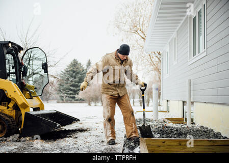 Mann hält Schaufel im Hinterhof gegen Himmel arbeiten im Winter Stockfoto