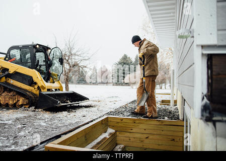 Seitenansicht der Mann hält Schaufel arbeiten im Hinterhof gegen Himmel im Winter Stockfoto