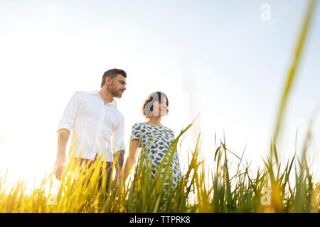 Low Angle View der Mann mit schwangeren Frau auf Wiese gegen den klaren Himmel Stockfoto