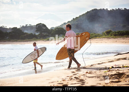 Seitenansicht der männlichen Surfern, die surfbretter beim Spaziergang am Strand. Stockfoto