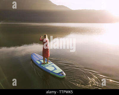 Eine weibliche paddleboarding auf einem See bei Sonnenaufgang Stockfoto