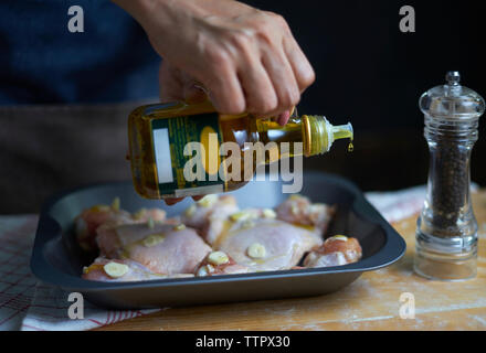 Mittelteil der Frau gießen Olivenöl auf Hühnerfleisch in Fach Stockfoto