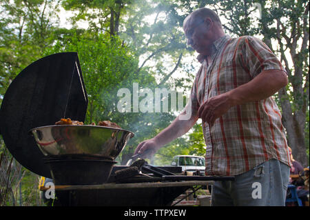 Low Angle Sicht des Menschen kochen Hähnchen auf Grill im Wald Stockfoto