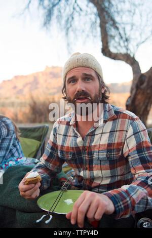 Porträt der Mann mit unordentlichen Mund halten s'More im camp site Stockfoto