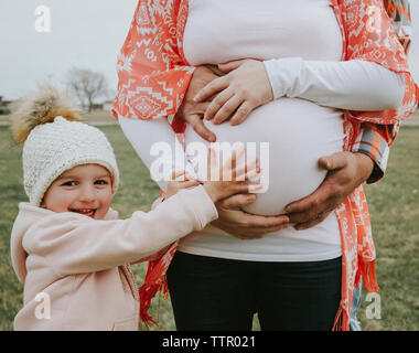 Portrait von fröhlichen Tochter schwanger Bauch der Mutter zu berühren mit dem Vater auf dem Feld Stockfoto