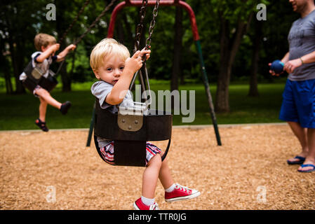 Untere Partie der Vater mit Kindern geniessen Sie Schwingen in der Spielplatz Stockfoto