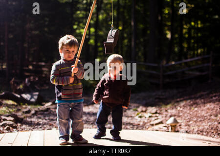 Jungen auf der Suche nach Bruder Holding künstlichen Fisch in Spielplatz Stockfoto