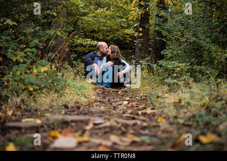 Paar küssen beim Sitzen auf dem Feld im Wald Stockfoto