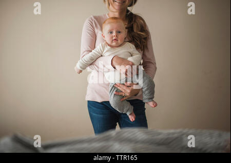 Mittelteil der Mutter mit Baby Boy, während gegen die Wand zu Hause stehend Stockfoto