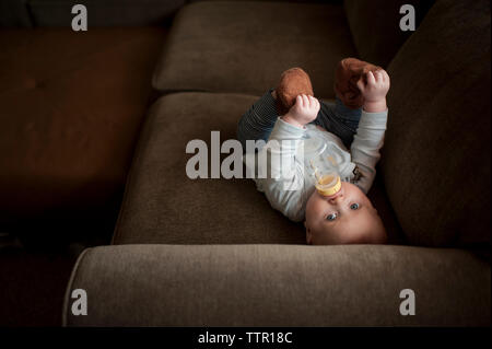 Hohen winkel Portrait von baby boy das Trinken der Milch aus der Flasche, während auf dem Sofa zu Hause liegen Stockfoto