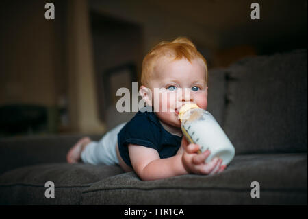 Portrait von cute baby boy das Trinken der Milch aus der Flasche, während auf dem Sofa zu Hause liegen Stockfoto