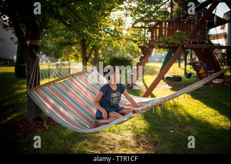 Nachdenkliches Mädchen weg schauen, während auf der Hängematte am Spielplatz sitzen Stockfoto