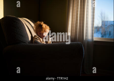 Baby Boy spielen mit Spielzeug, während auf der Couch zu Hause sitzen bei Sonnenuntergang Stockfoto