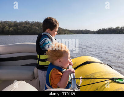 Gerne Brüder Schwimmwesten beim Stehen in der Boot auf See gegen den klaren Himmel während der sonnigen Tag Stockfoto