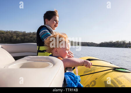 Brüder Schwimmwesten beim Stehen in der Boot auf See gegen den klaren Himmel während der sonnigen Tag Stockfoto