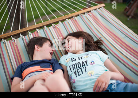 Hohe Betrachtungswinkel von Happy Geschwister sprechen, während Sie sich auf einer Hängematte im Hof Stockfoto