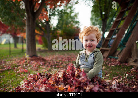 Porträt der süße kleine Junge sitzt im Blatt Haufen im Hinterhof zu Hause Stockfoto