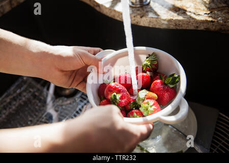 Zugeschnittenes Bild der Hände waschen Erdbeeren im Sieb Stockfoto