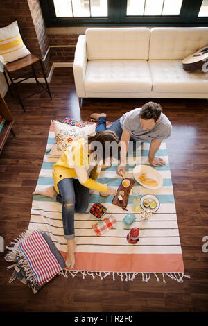 Hohe Betrachtungswinkel von Paar Essen während der Sitzung auf dem Teppich zu Hause Stockfoto