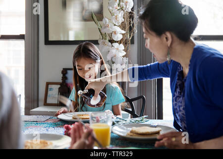 Mutter gießen Ahornsirup auf Pfannkuchen für Tochter beim Frühstück Stockfoto