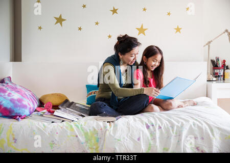 Mutter und Tochter lesen Buch beim Sitzen auf dem Bett zu Hause. Stockfoto